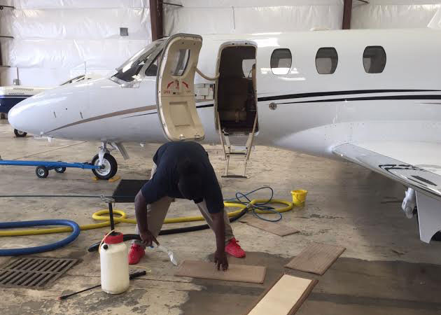 A person bent over while cleaning floor mats with an airplane in the background