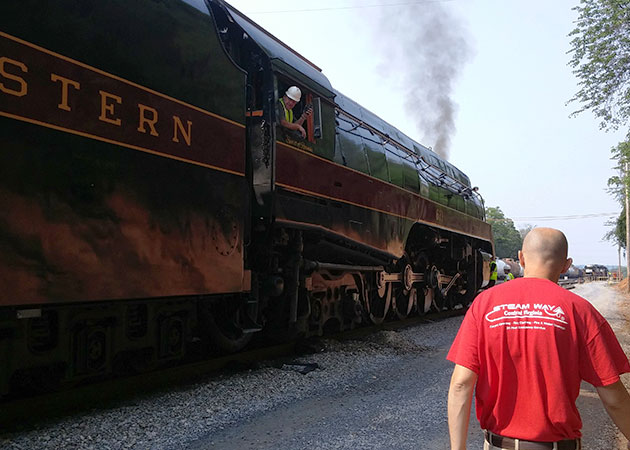 A person wearing a red shirt as he's walking next to a train
