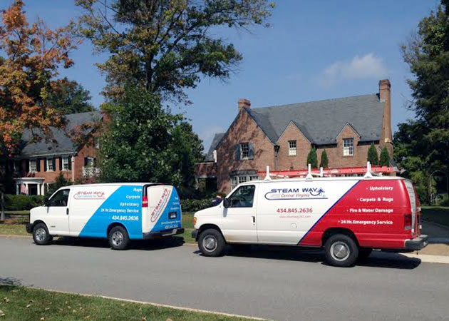 Two vans parked on a street in front of two brick homes